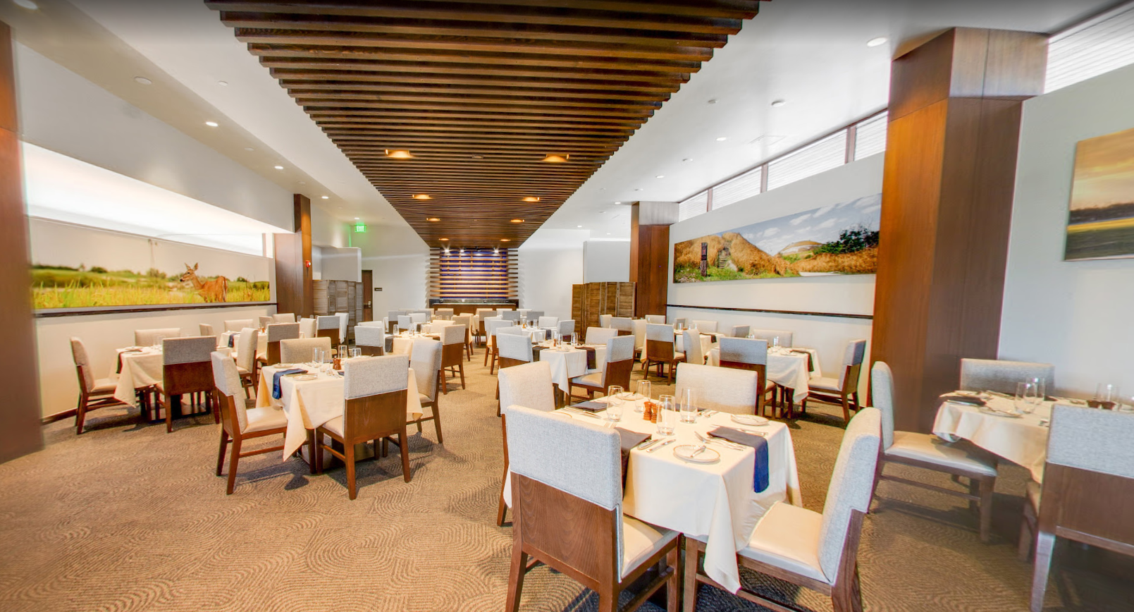 Fin & Feather dining room with white-clothed tables, modern wood slat ceiling, and scenic landscape wall art.