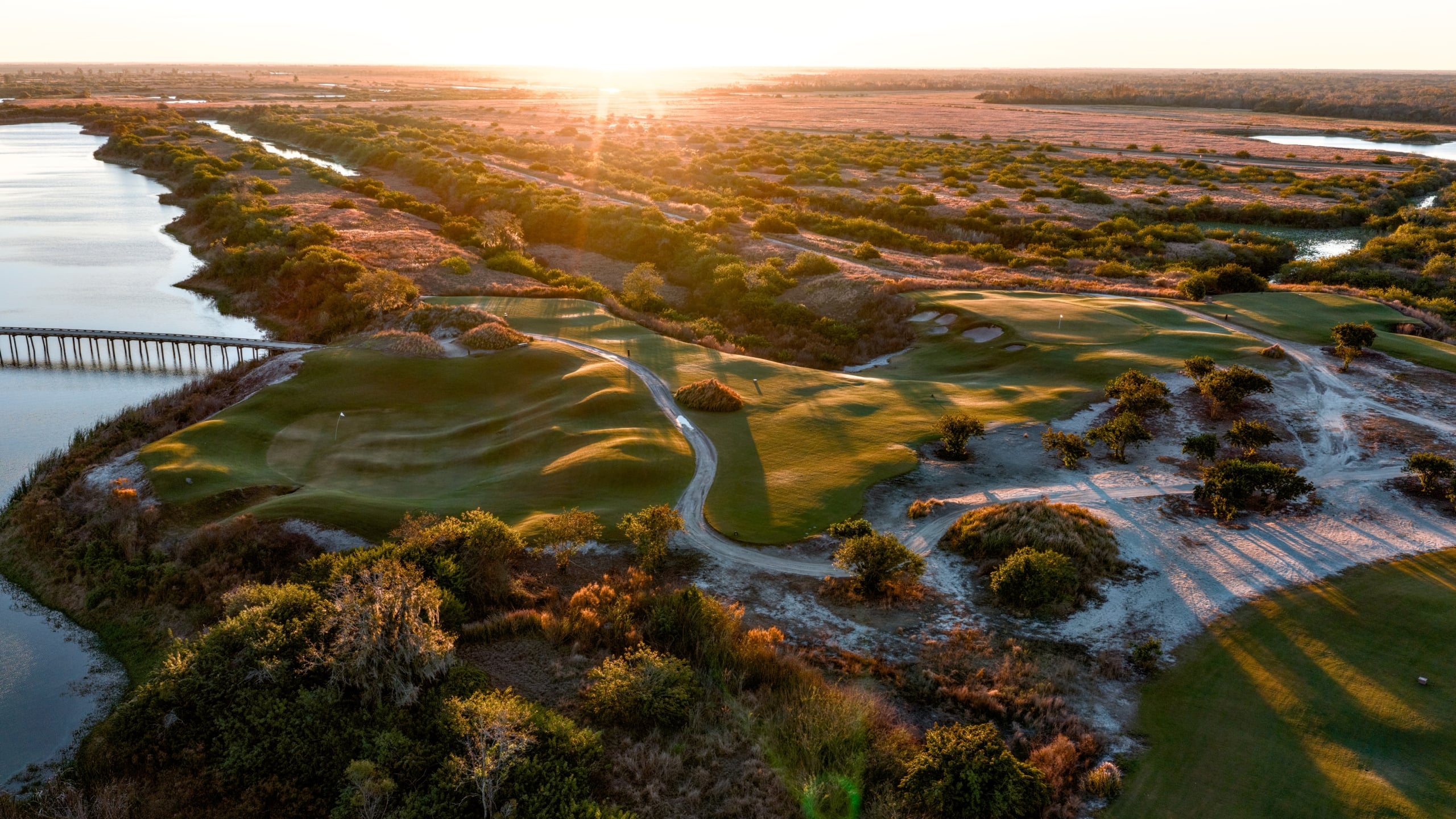 Aerial view of the 11th hole of the Chain golf course at Streamsong Resort at dusk, with a bridge over a large river