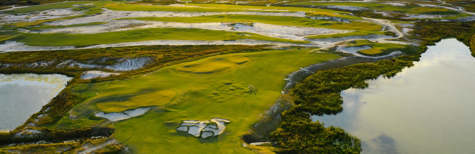 A golf course with calm waters, bunkers, and green grass