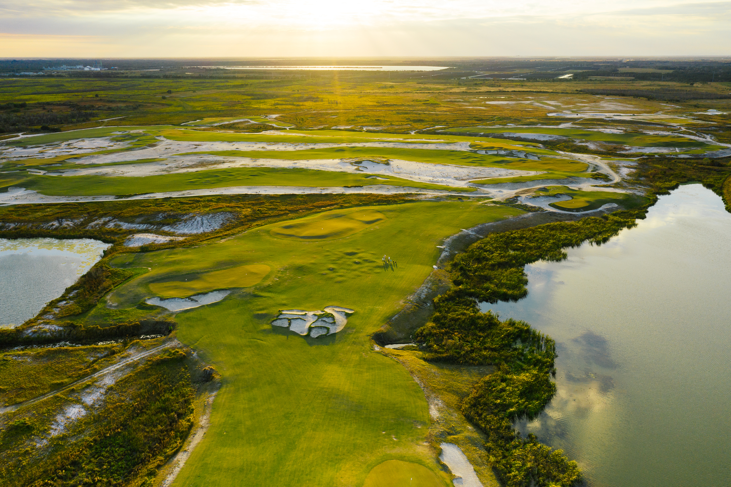 A golf course with calm waters, bunkers, and green grass