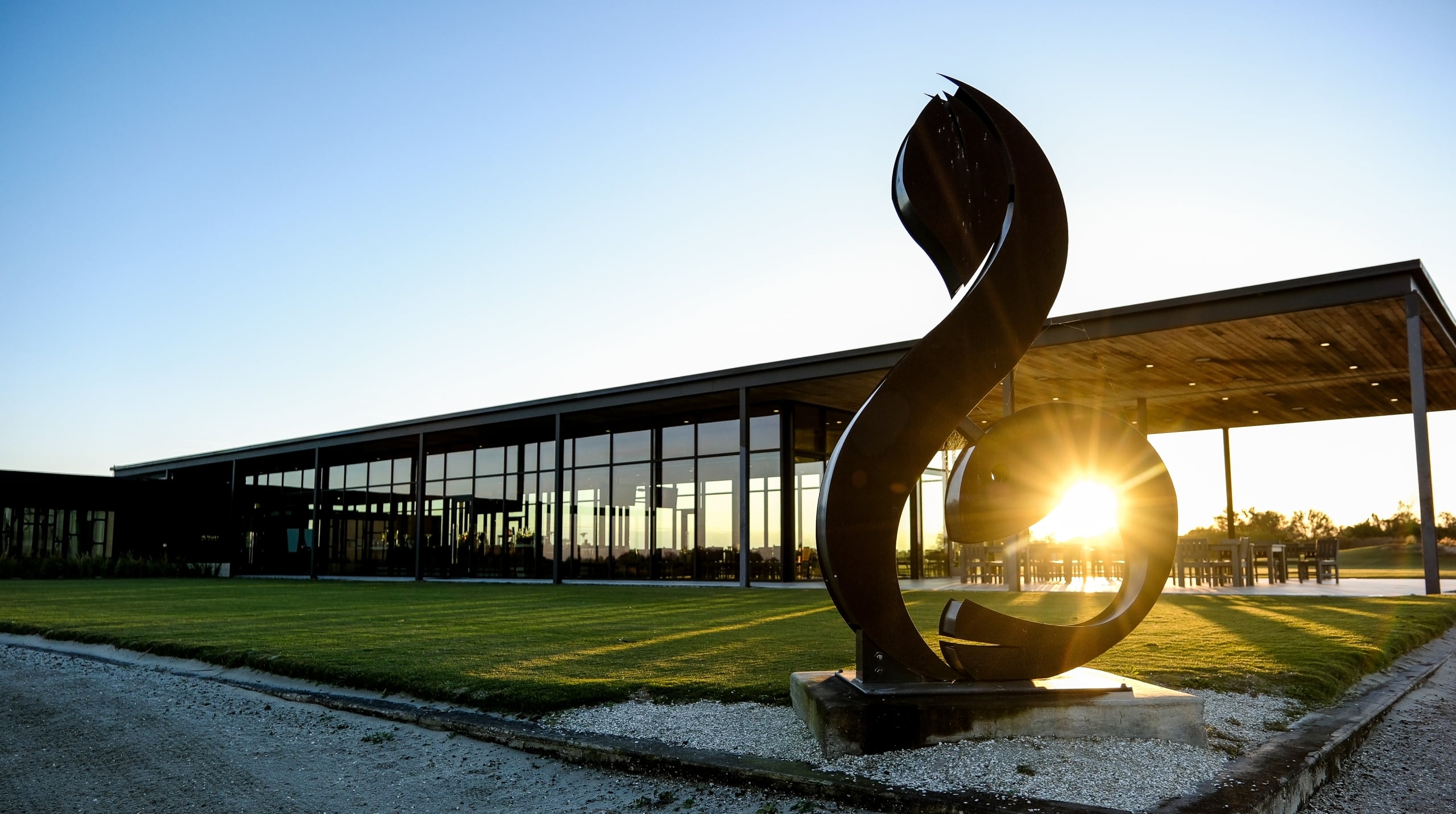 Modern golf pavilion at Streamsong Resort with a large metal sculpture silhouetted against a bright sunset.