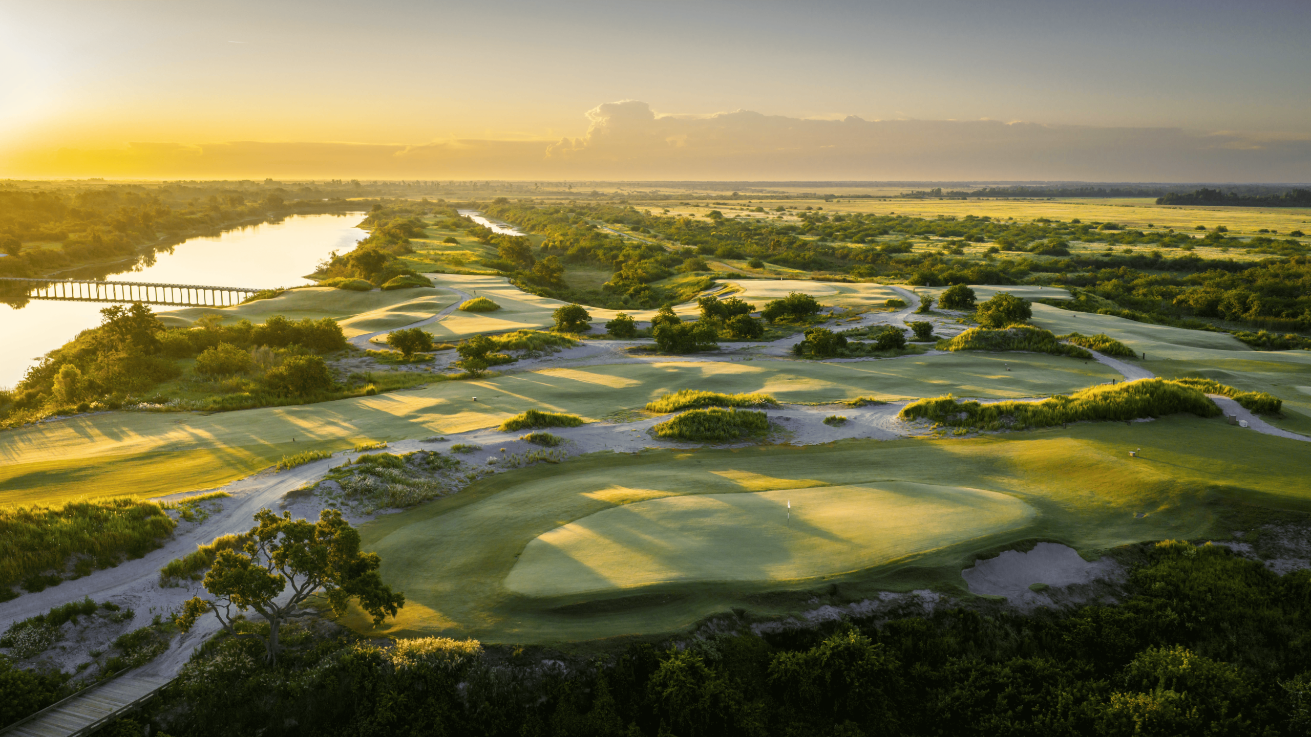 High-angle golden hour view of a winding golf course green nestled between a lake and wild Florida marshland.