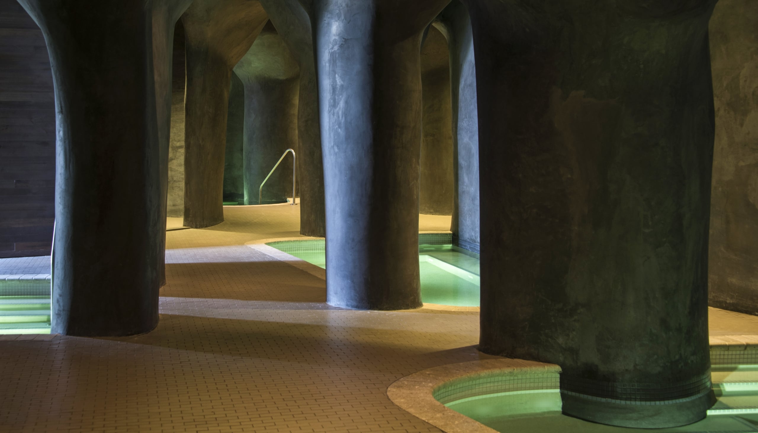 Dimly lit grotto-style spa area at Streamsong with organic concrete columns and glowing turquoise water pools.