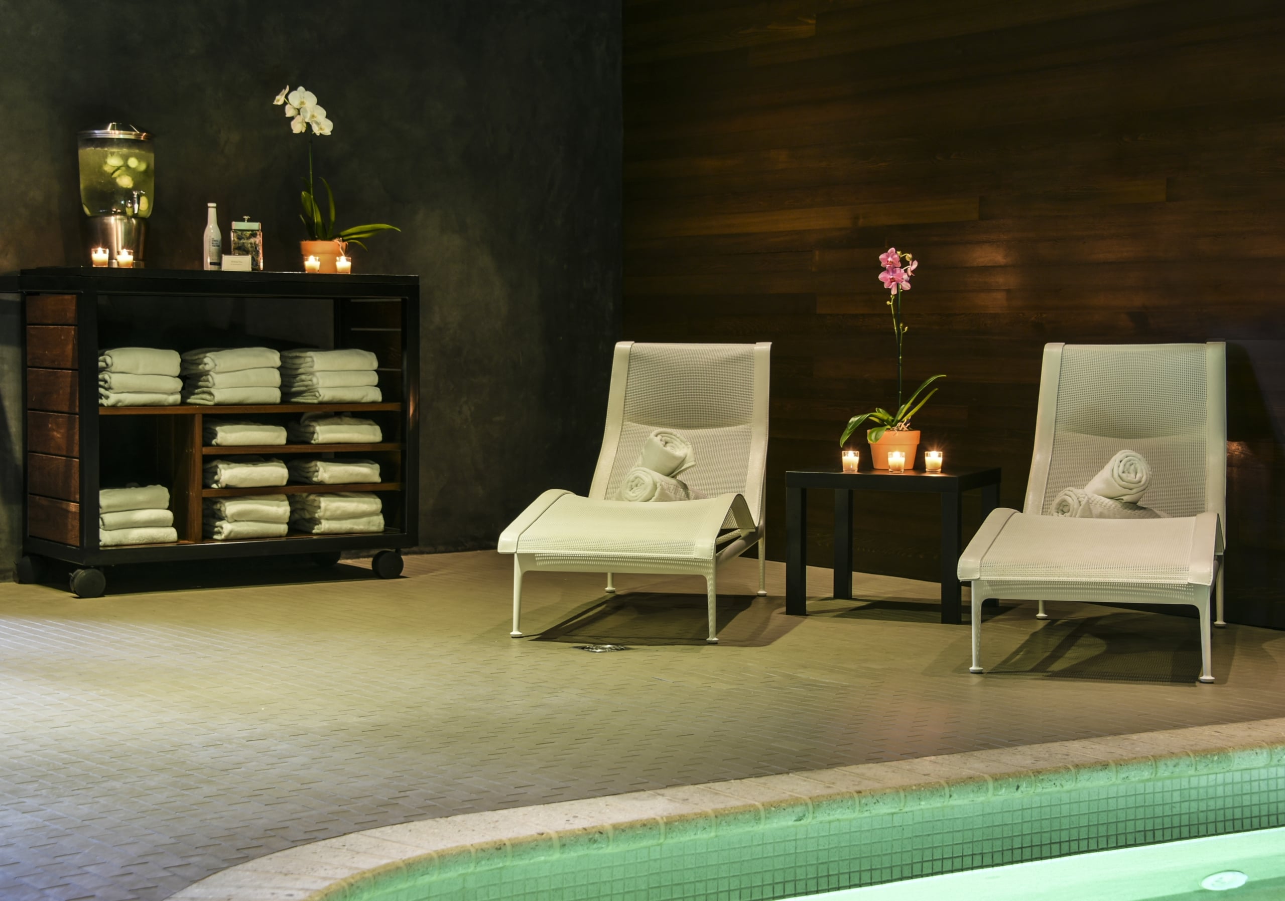 Relaxation area at AcquaPietra Spa with white lounge chairs, candlelight, orchids, and a refreshment station.
