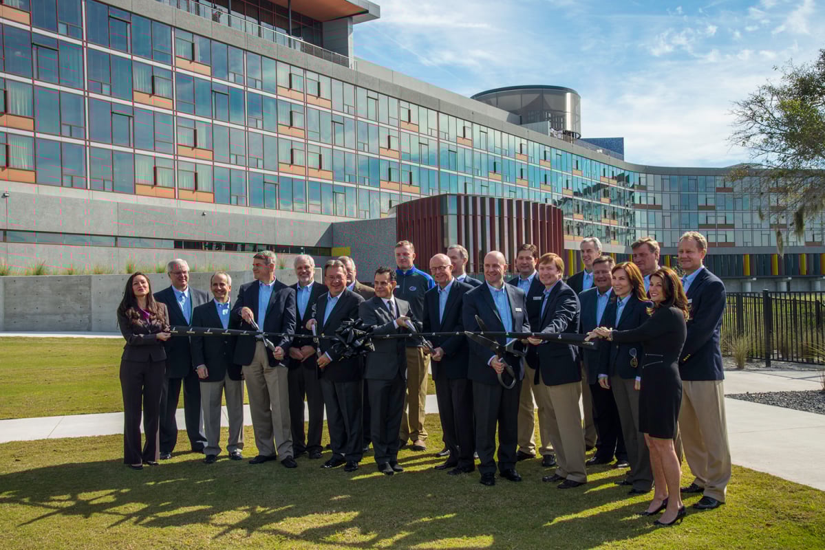 Large group of executives holding giant scissors for a ribbon-cutting ceremony in front of the modern Lodge at Streamsong.