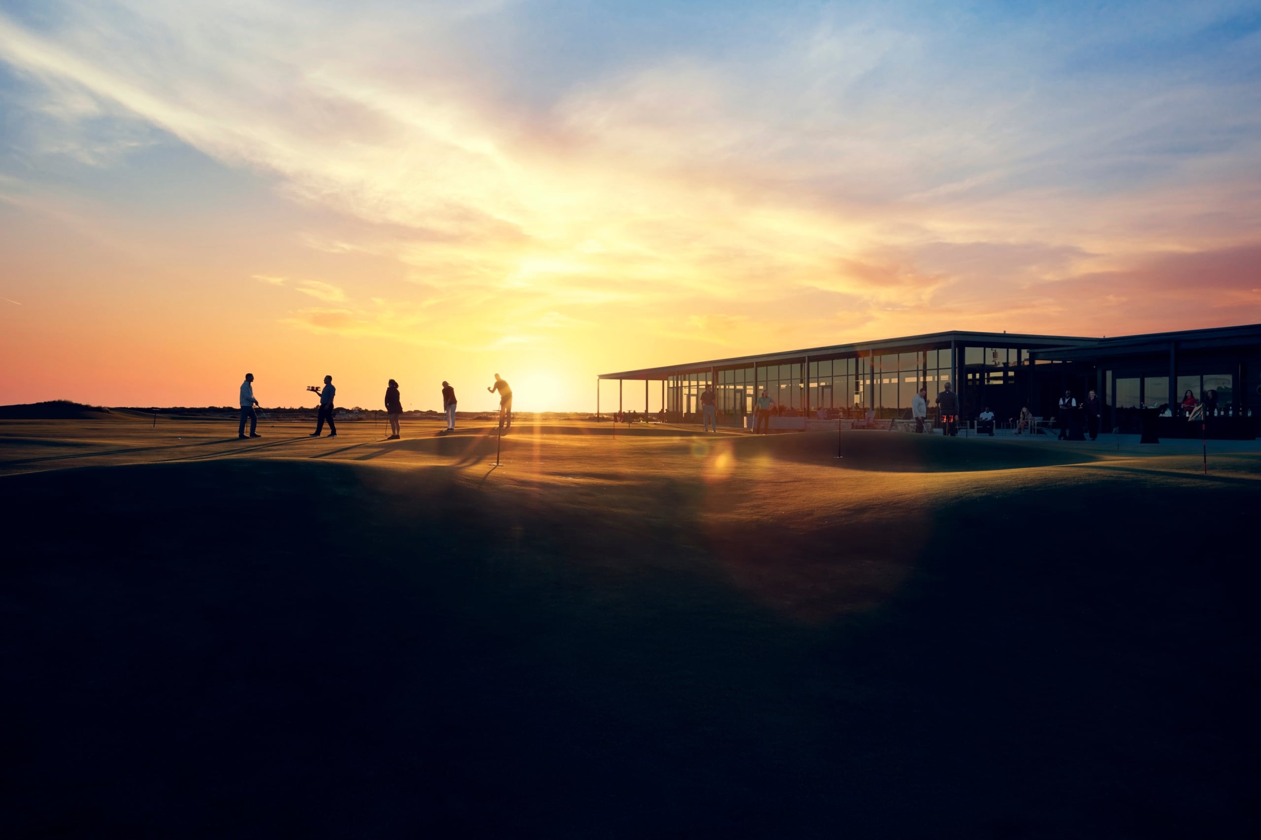 Golfers putting next to the clubhouse at sunset